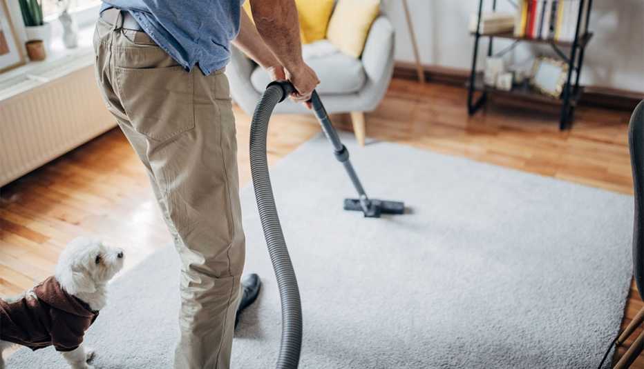 a man vacuums a rug in front of his dog