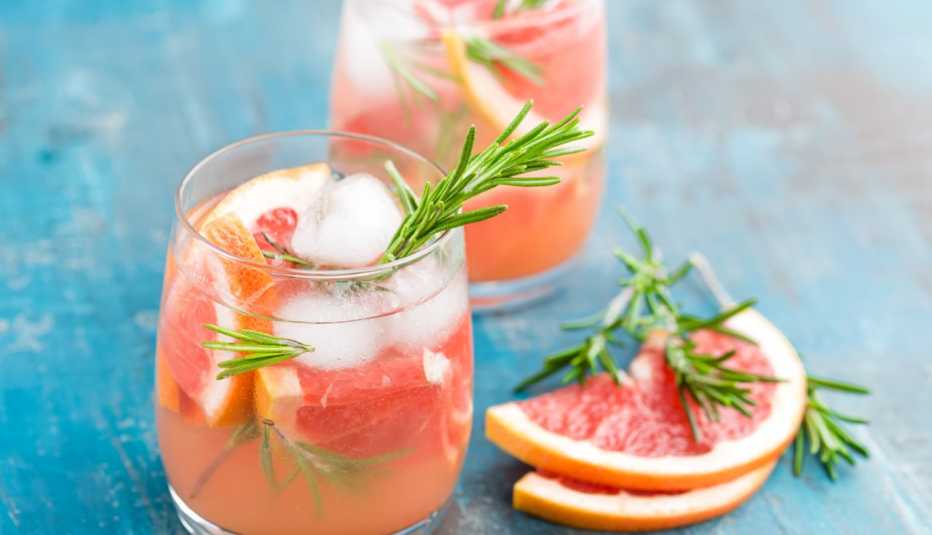 Two mixed drinks with fruit sitting on a blue wood table