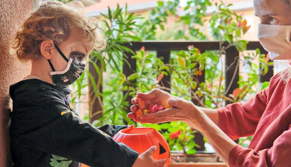 a masked adult puts candy in the basket of a masked trick or treater child