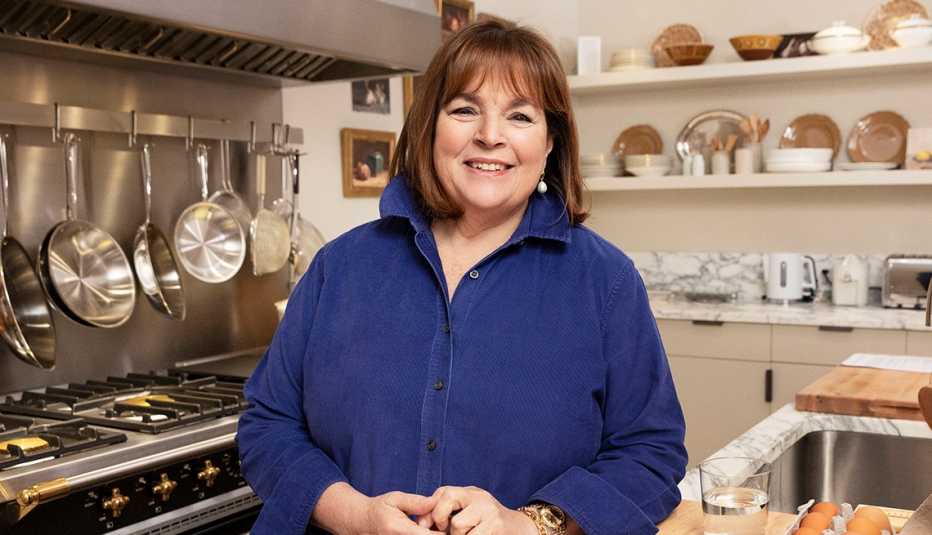 Ina Garten, chef, in blue long sleeve button up blouse, kitchen stove, white shelves, marble backsplash