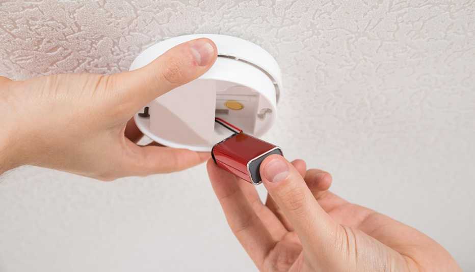 hand holding smoke detector on ceiling; another hand holding battery beneath it