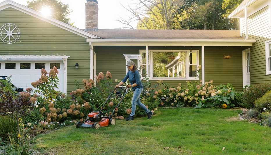 green house with flowers surrounding it and woman mowing lawn