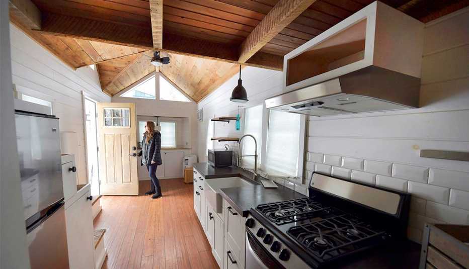A woman looks out the front door, standing inside of a tiny home
