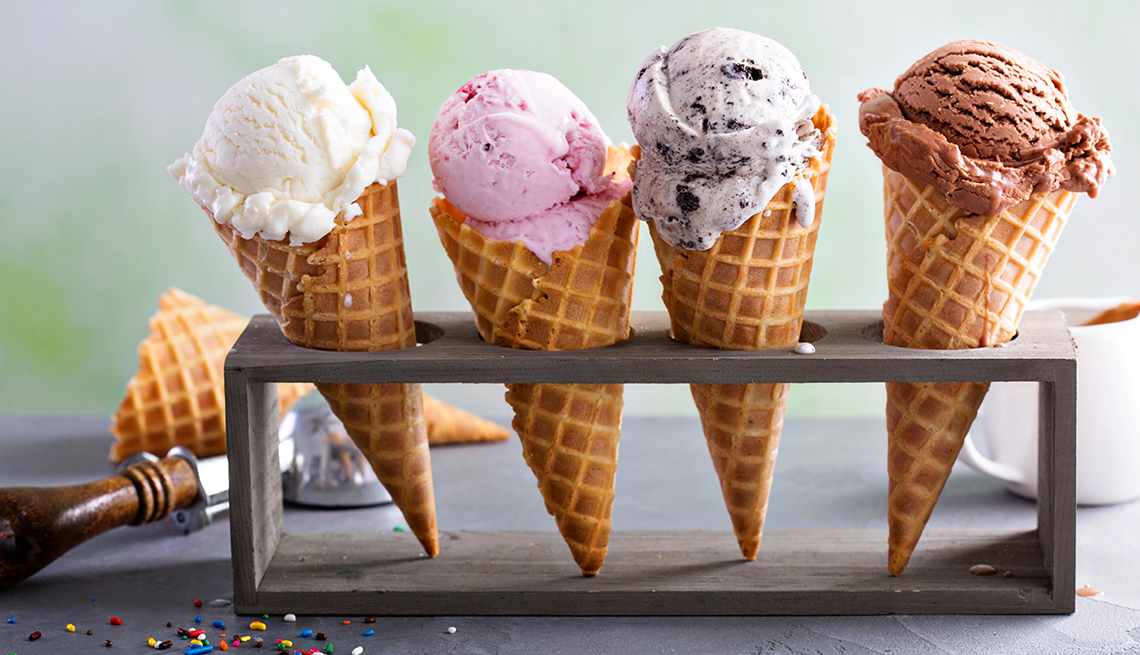 four ice cream cones of different flavors vanilla strawberry cookies and cream and chocolatein in a cone holder 