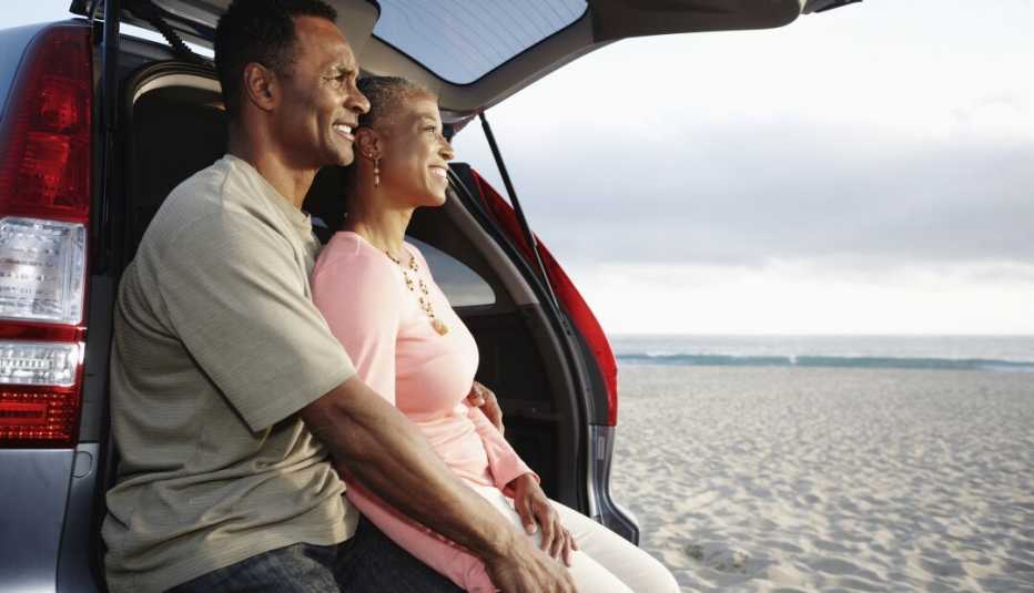 Couple sitting in the back of a car looking out at the ocean.