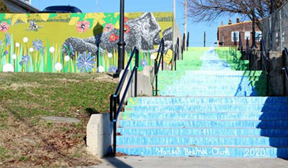 An outdoor staircase is painted sky blue, white and bright green, a mural in the background features flowers and a gorilla
