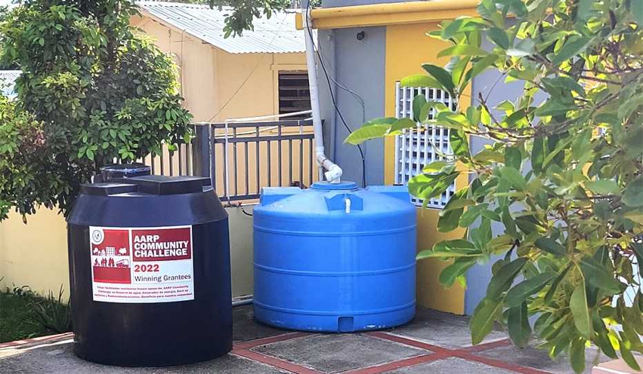 Two rainwater barrels, one displaying the AARP Community Challenge logo