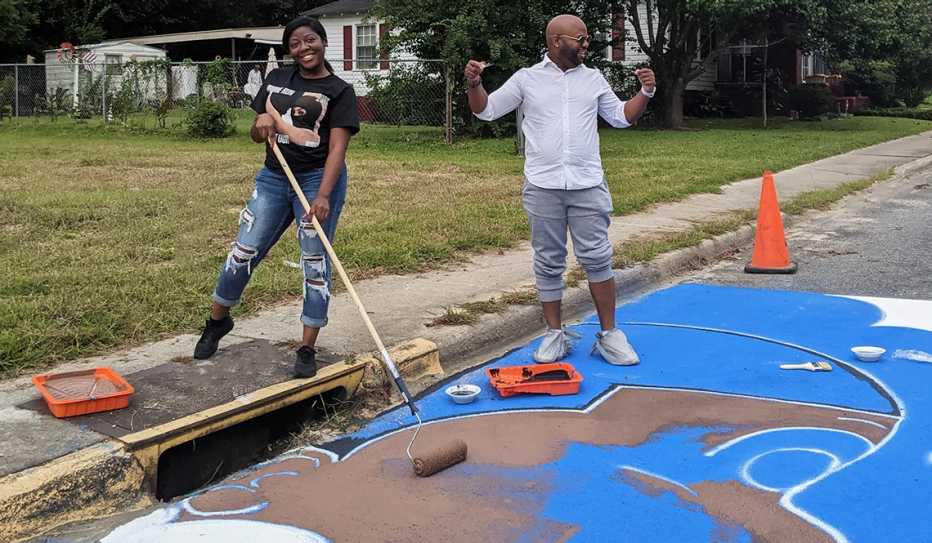 A woman and man paint a mural on a street in a residential neighborhood