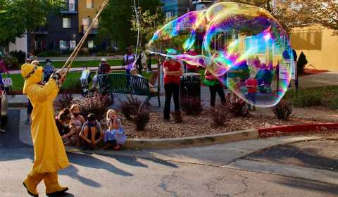 A person wearing yellow raingear makes giant bubbles with a bubble wand