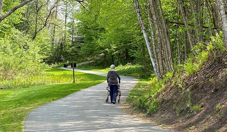 An older woman pushes a wheeled walker while she travels along a multiuse recreation trail An older woman pushes a wheeled walker while she travels along a multiuse recreation trail