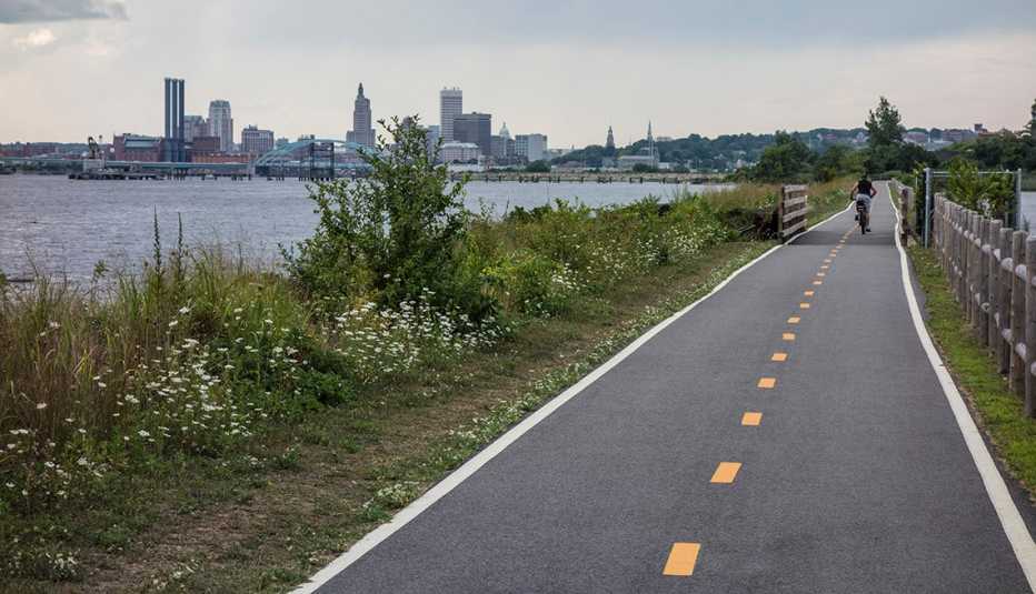 Bicyclist, Bike Path, City Skyline In Background, Providence, Rhode Island Complete Streets Plan, AARP Livable Communities The East Bay Bicycle Path leads to Providence, Rhode Island, and is a popular spot for bicycle commuting.