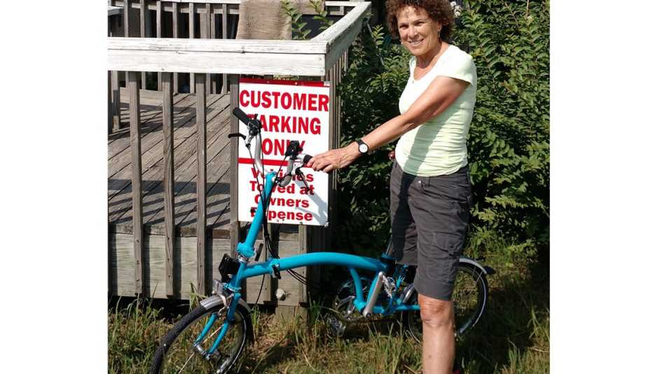 Woman Stands Next To Her Foldable Bike And Poses Next To Sign About Customer Only Parking Towing Sign, Livable Communities, Biking Infrastructure