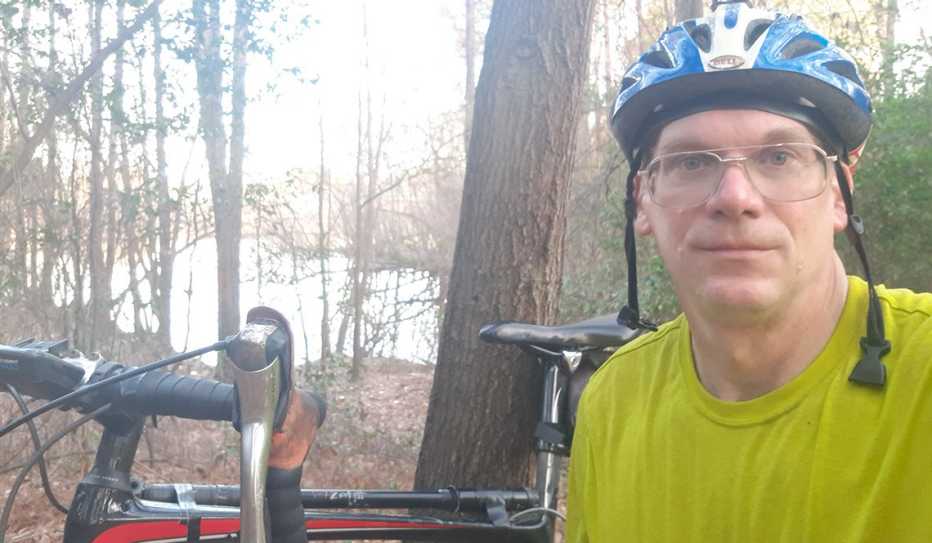 David Maryniak taking a break from a bike ride in a woods near a lake