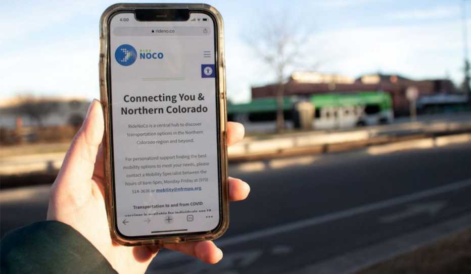 A person holds a phone showing the RideNoCo website