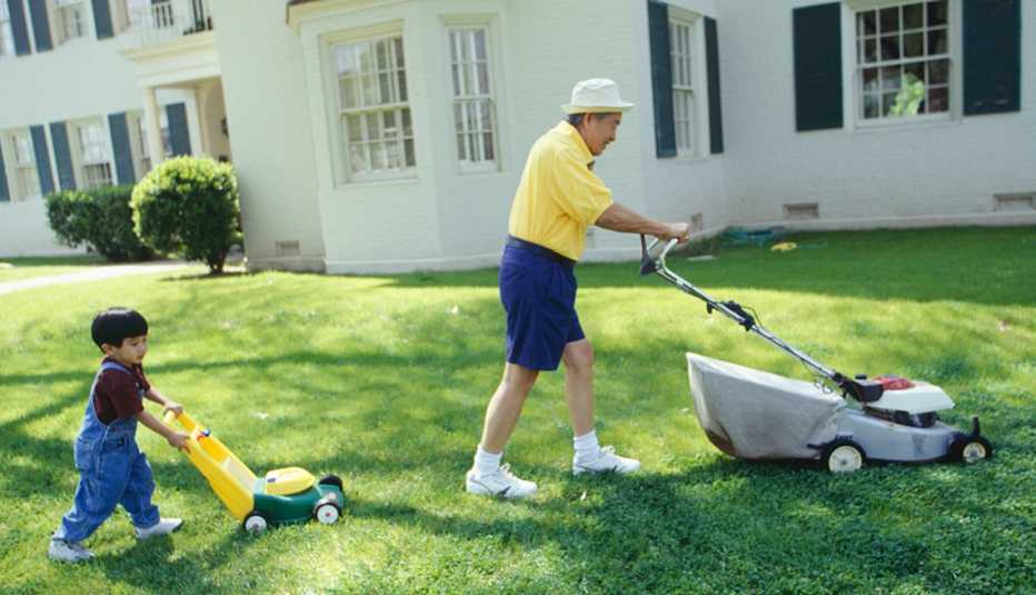 Grandfather and grandson (3-4) mowing lawn in garden, side view