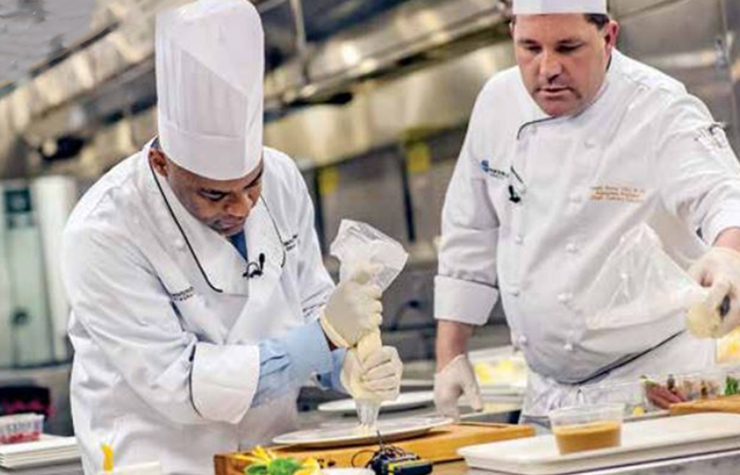 Michael Hancock, Mayor of Denver, Colorado, shown wearing a chef's uniform and learning how to work in a restaurant kitchen.
