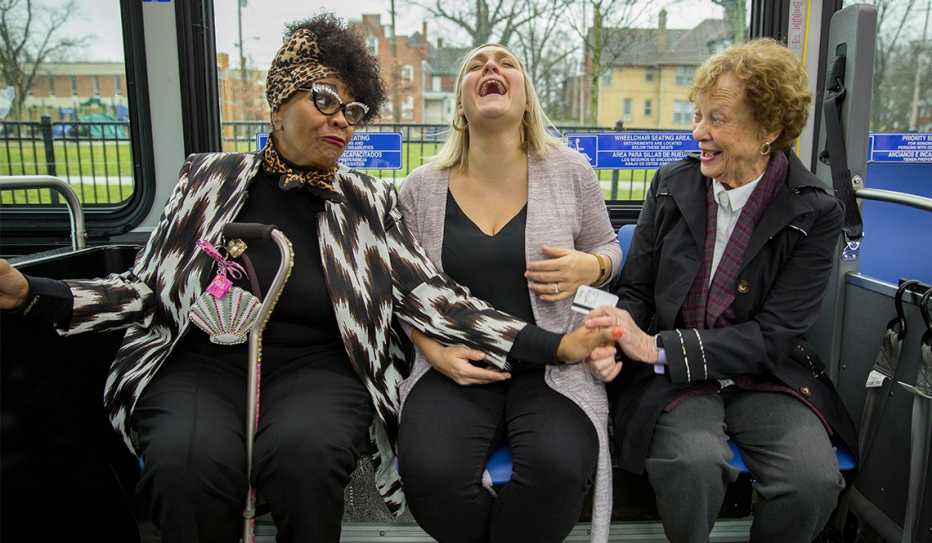 Two older women and a young woman share a laugh while sitting on a bus