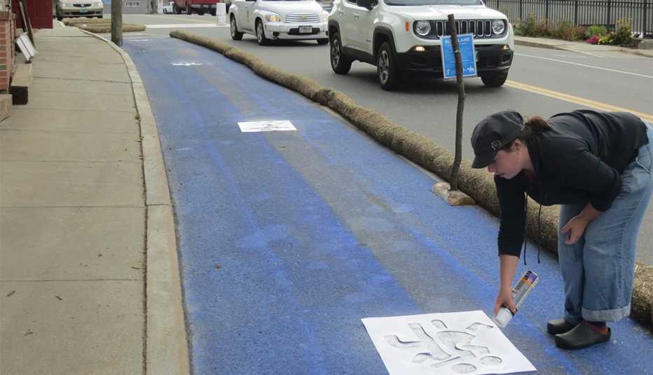 A woman uses a stencil and white spray paint to add markings to the Blue Lane.