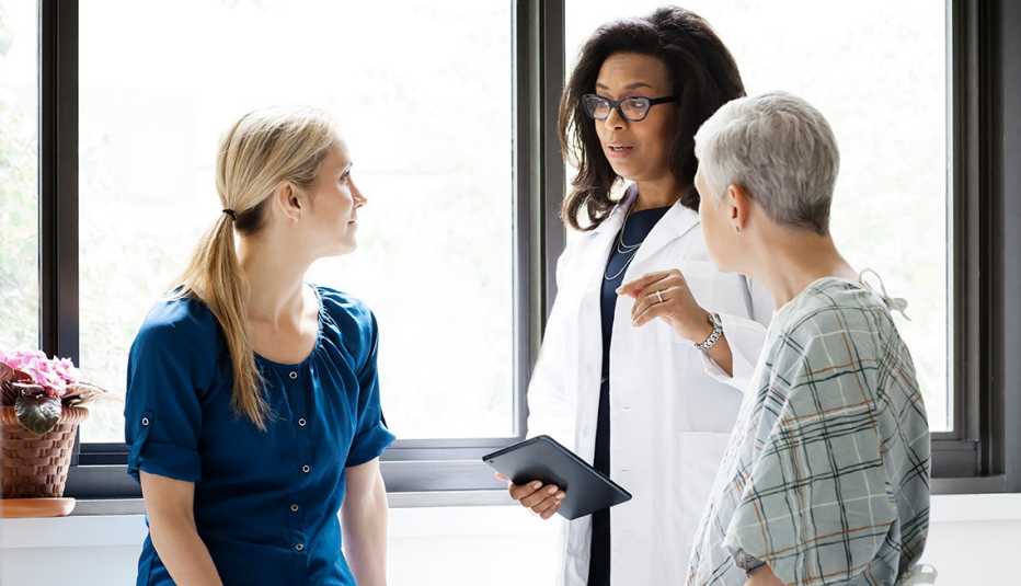 A woman in a medical gown and her adult daughter talking to a physician in a doctors office