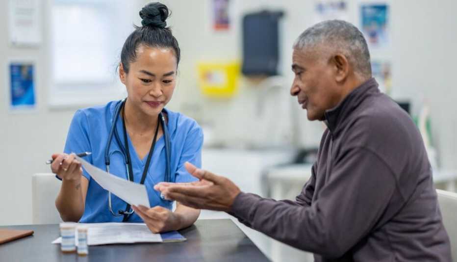a man sitting at a table talking to a doctor who is showing him paperwork