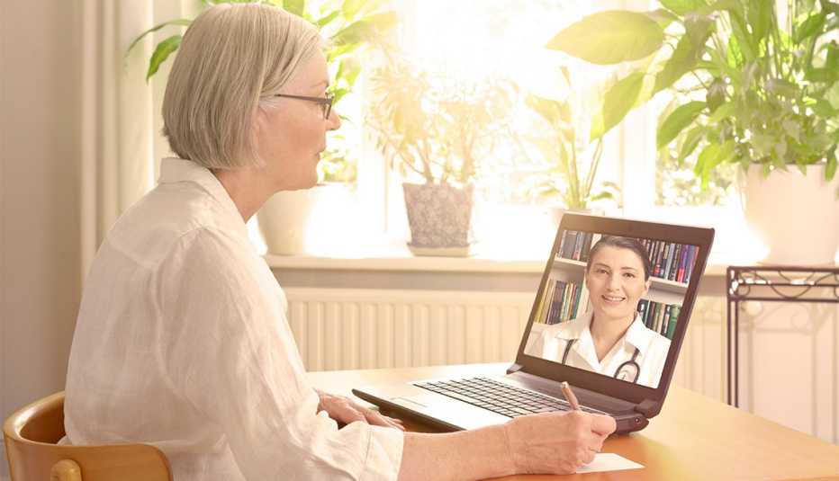 Woman in front of a laptop taking  notes during a video call with her female doctor