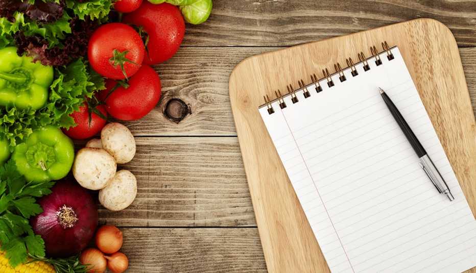top view of notebook and cutting board with raw vegetables around it