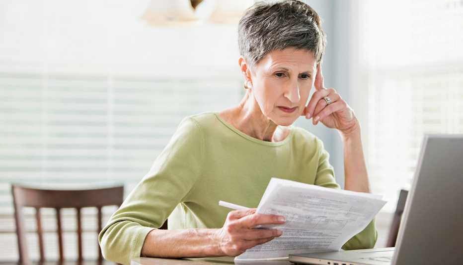 woman looks at papers as she sits in front of a computer