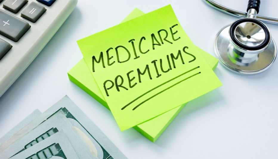 sticky note that says Medicare Premiums with a calculator, a few hundred-dollar bills, and stethoscope sticky note that says Medicare Premiums with a calculator, a few hundred-dollar bills, and stethoscope