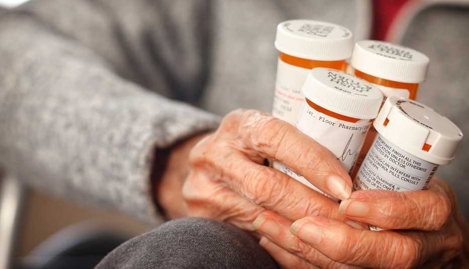 close up of hands holding four prescription pill bottles