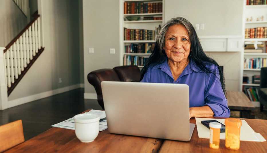 a woman sitting at a table using a laptop computer. A file folder and prescription bill bottles sit next to her