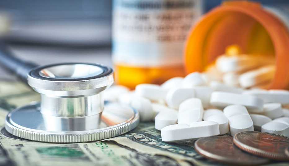 A stethoscope and prescription medication laid on top of dollar bills and coins