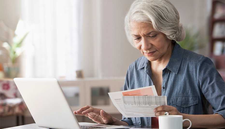 Woman sits at a table, holding bills and working on a computer Woman sits at a table, holding bills and working on a computer