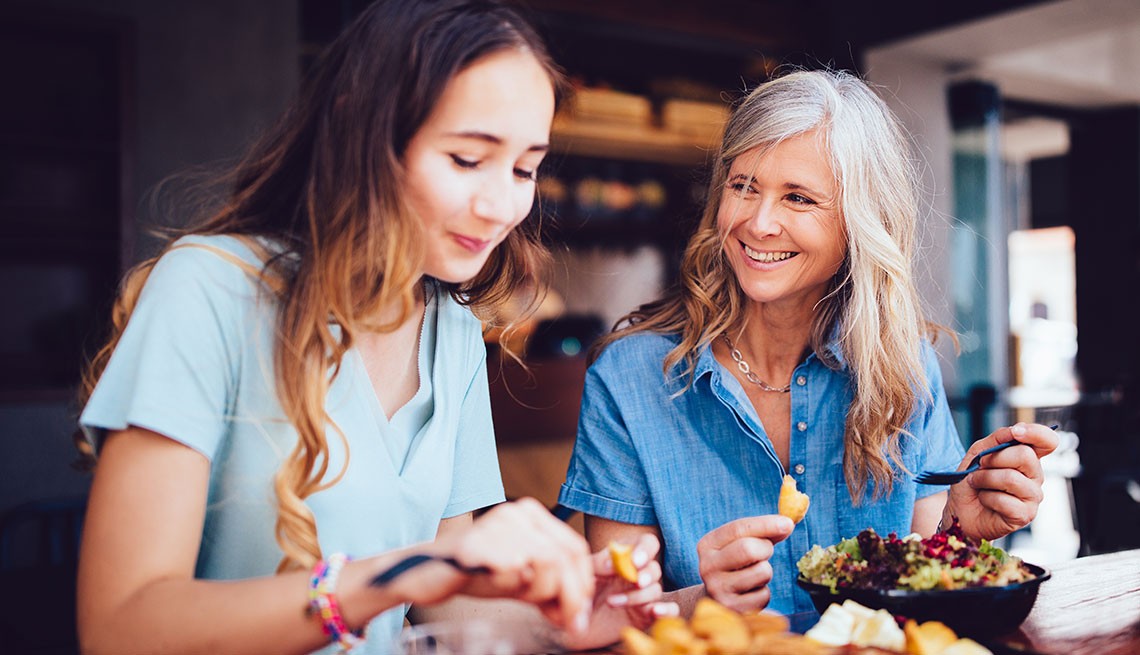 two women, older and younger, mom and daughter, sitting at restaurant bar counter, eating and smiling