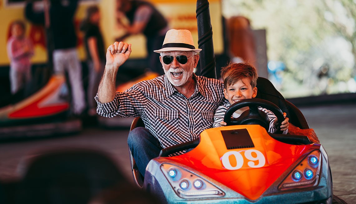 grandfather wearing sunglasses and plaid shirt with hat on and grandson riding in an orange with the number 9 on it go-cart smiling 
