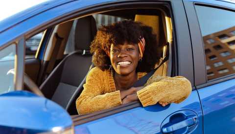 Save on Car Rentals woman smiling in driver side of a blue car, she is wearing a yellow sweater