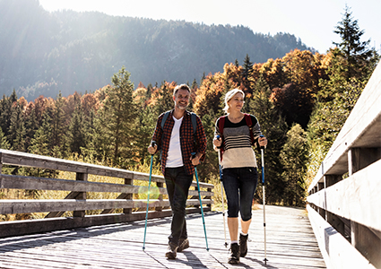 Middle aged couple hiking over a bridge with fall foliage in the background
