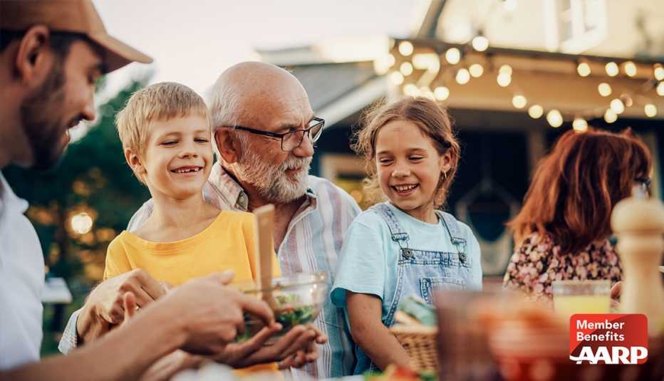 AARP member enjoying a meal outdoors surrounded by family and smiling grandchildren in late summer 