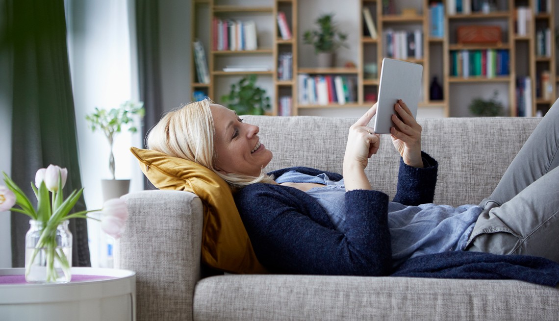 Woman relaxing on a grey couch reading books from the Libby Library app her tablet