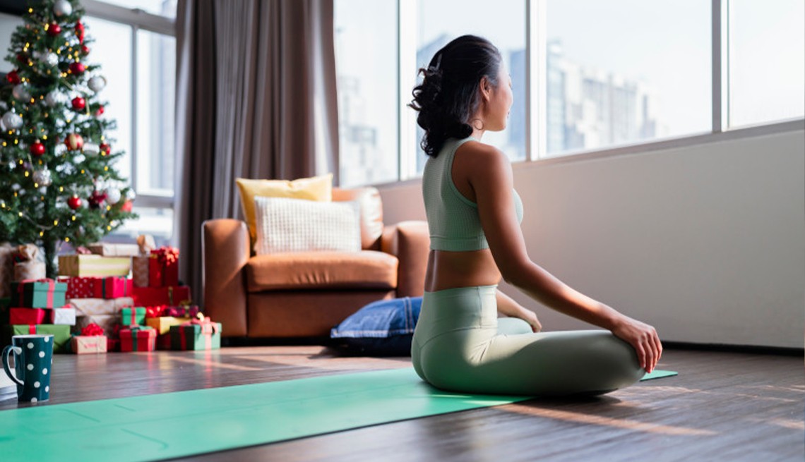 AARP member doing yoga in her living room with Christmas tree in the background.
