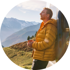 Man detressing holding a tea cup and looking serene with scenic mountains in the background