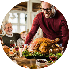 Man in a maroon sweater bringing Thanksgiving turkey to the family dinner table