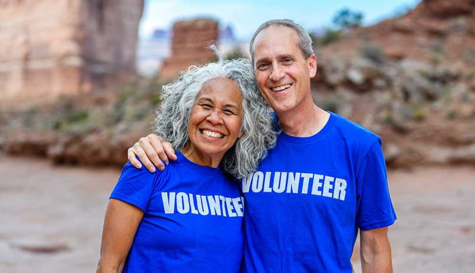 Man and woman wearing blue shirts that say volunteer on them smiling and posing for a photo together outdoors