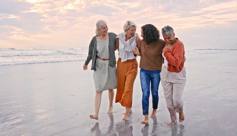 Group of AARP members hugging and walking on a beach together at sunset while on vacation