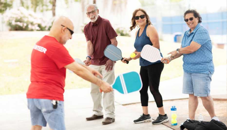 Group of AARP members taking a pickleball class together outdoors led by volunteer in red shirt