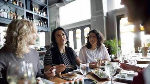 three women facing three women across a restaurant table during the day talking, smiling and eating sushi