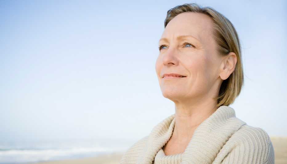 Serene looking woman wearing a white sweater look off into the distance on a pristine beach