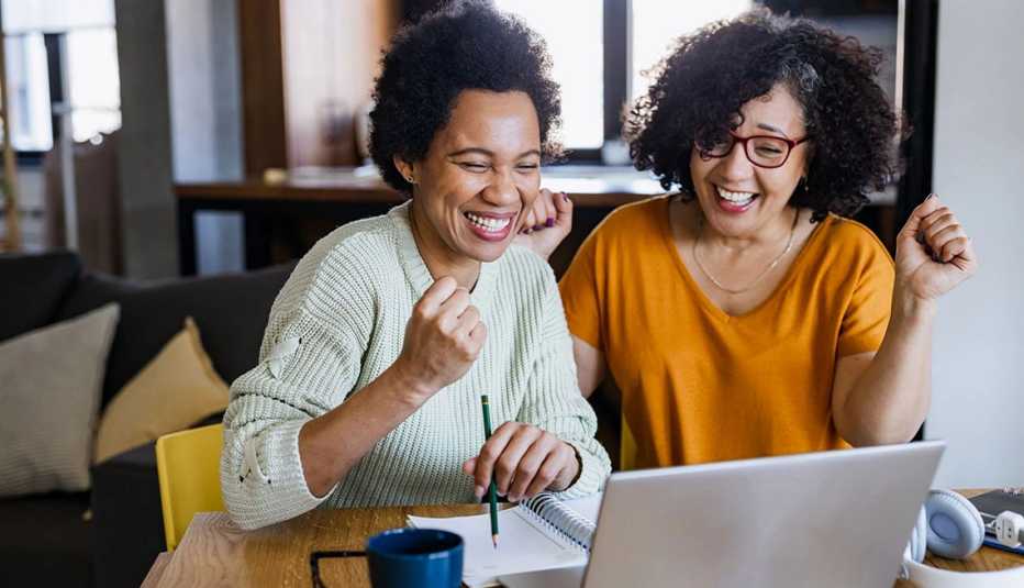 Two women sitting at a table, looking at a laptop smiling and cheering