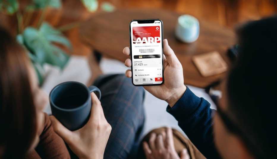 A man holding a mobile phone showing a digital AARP member card through the AARP Now app.