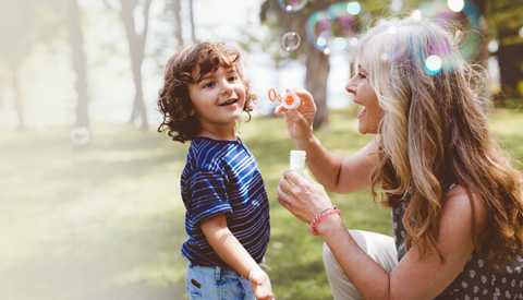 a woman and child in a park blowing bubbles
