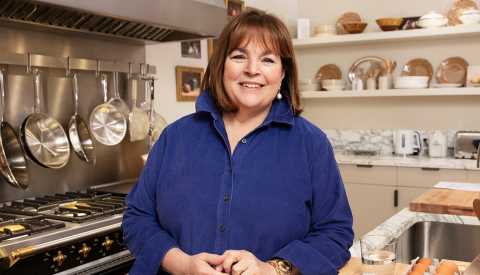 Ina Garten, chef, in blue long sleeve button up blouse, kitchen stove, white shelves, marble backsplash